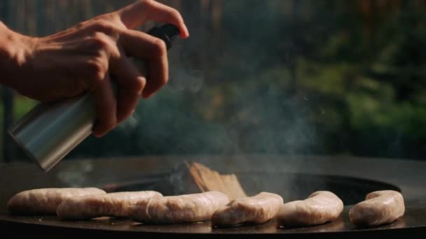 Шеф-кухар розпилює олію на ковбасах на задньому дворі. Чоловік готує ковбаски на вулиці . — стокове відео