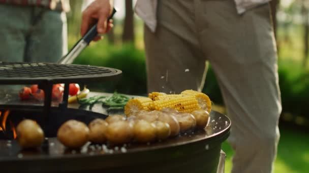 남성 요리사는 야외에서 음식을 요리하기 위해 겸자를 사용 한다. 사람들 이 bbq 에 소금을 붓는 모습 — 비디오