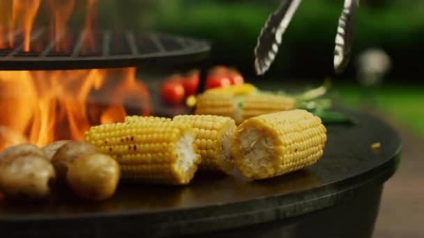 Zöldségeket grillezünk odakint. Férfi kéz csipeszes kukoricát forgat — Stock videók