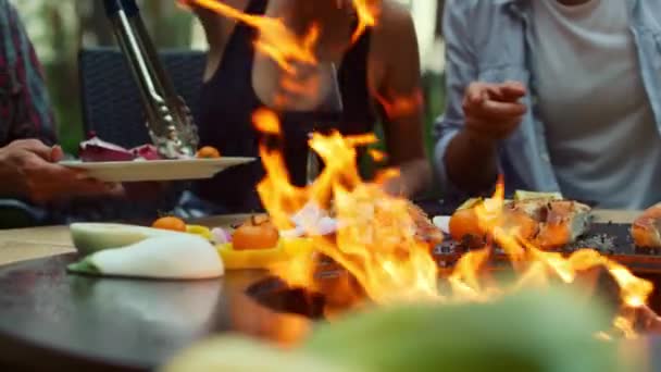 Donna bionda che usa il forcipe in giardino. Amici che preparano pesce e verdure — Video Stock