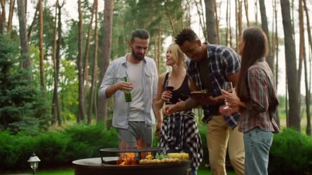 Freunde verschiedener Rassen plaudern im Hinterhof. Mann kocht Gemüse auf Grill — Stockvideo