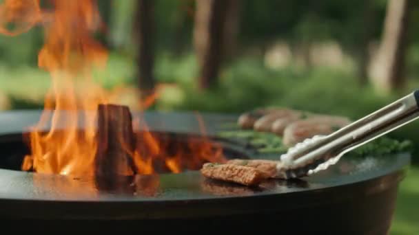 Muž vaří velké maso na grilu venku. Muž dává masové tyčinky s kleštěmi — Stock video