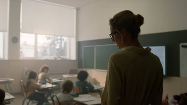 Öğretmen sınıfta öğrencilerle konuşuyor. Okul çocukları birlikte okuyorlar. 