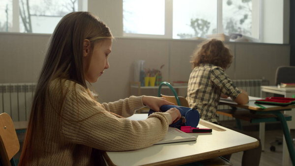 Cheerful girl sitting at desk in school. Focused student learning in classroom