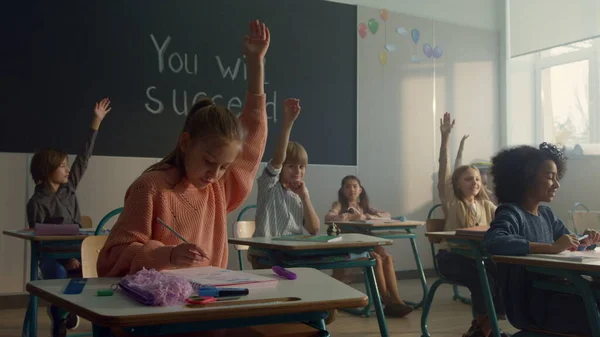 Niños sentados en escritorios en clase. Alumnos inteligentes levantando las manos en la lección —  Fotos de Stock