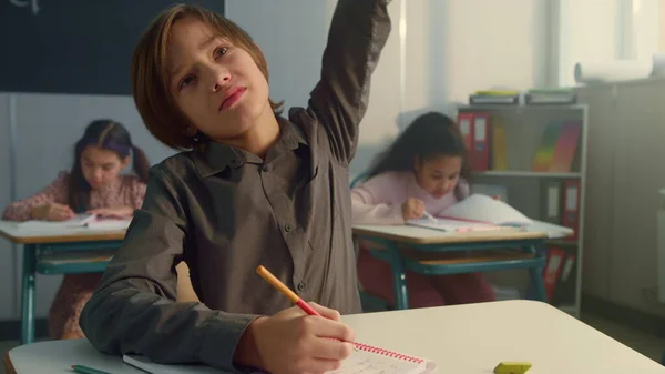 Rapaz a levantar a mão durante a aula na escola primária. Escrita estudantil em caderno — Fotografia de Stock