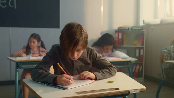Schooljongen schrijft in notitieboekje bij de les. Bedachtzame jongen met pen in de mond — Stockfoto