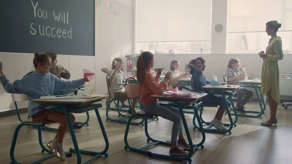 Estudiantes sentados en escritorios en clase. Alumnos jugando con aviones de papel —  Fotos de Stock