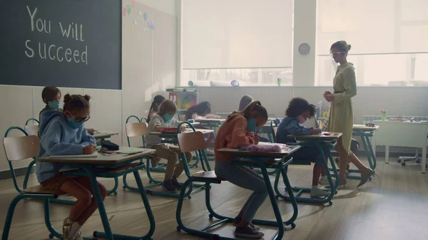 Niños con máscaras médicas estudiando juntos en el aula durante la pandemia del coronavirus —  Fotos de Stock