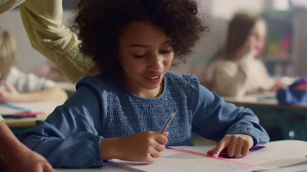 Meisje aan het praten met de leraar in de klas. Glimlachend schoolmeisje schrijven in notebook — Stockfoto