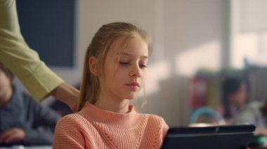 Dijital tablet kullanan bir kız. Öğretmen öğrencinin okul ödevlerini yapması için yardım ediyor.