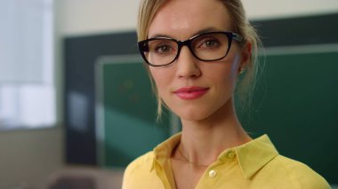 Öğretmen sınıfta kameraya poz veriyor. Yüzünde olumlu ifade olan kadın.