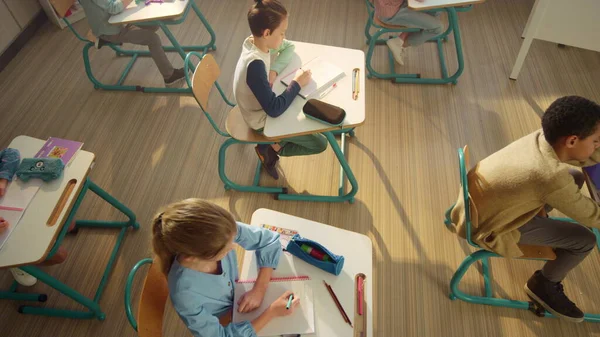 Alumnos sentados en escritorios en el aula. Niños y niñas escribiendo en cuadernos —  Fotos de Stock