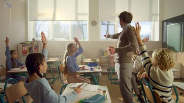 Öğrenciler sınıfta öğreniyor. Erkek öğretmen derste sorular soruyor.