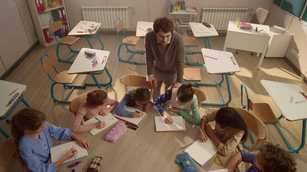 Profesor de escuela explicando la lección a los estudiantes. Niños inteligentes aprendiendo en el escritorio redondo — Foto de Stock