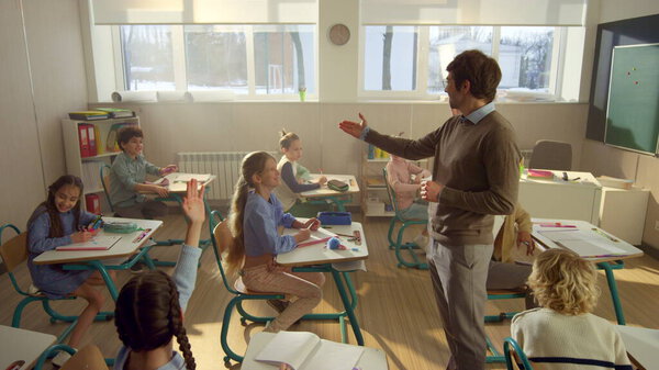 Teacher asking questions to students in class. Schoolchildren raising hands