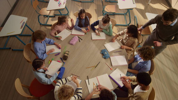 Mixed race children having lesson with teacher at round desk