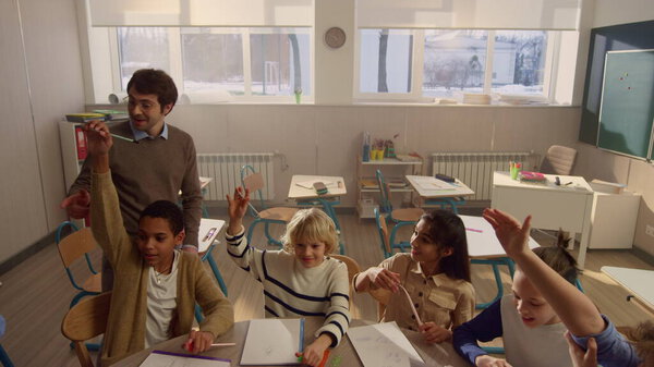 Students raising hands at lesson in classroom. Schoolteacher asking questions