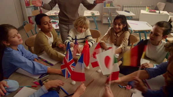 Multi ethnic students holding international flags in hands at round table