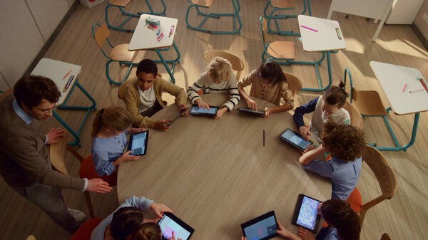 Male teacher helping students with tablet computers at lesson.
