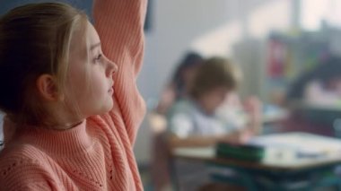 Sınıfta masa başında oturan bir kız. Akıllı öğrenci soru sormak için elini kaldırıyor.