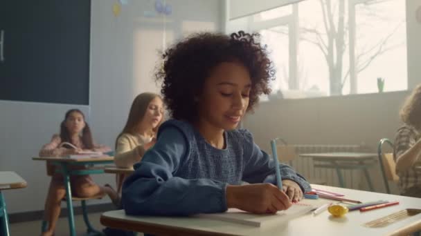 Menina sentada na mesa na sala de aula. Aluno alegre escrevendo no caderno — Vídeo de Stock