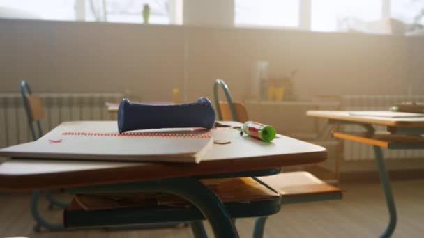 Iskolai kellékek hevernek az asztalon az osztályteremben. Jegyzetfüzet és tolltartó az asztalon — Stock videók