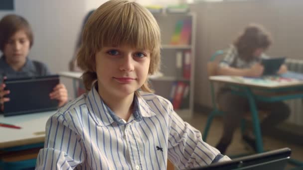 Student sedí za stolem s digitálním tabletem. Veselý chlapec pózující před kamerou — Stock video