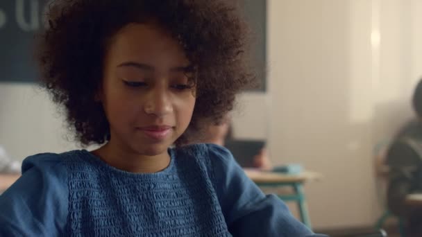 Vrolijk Afrikaans Amerikaans meisje zit aan het bureau met tablet computer op school — Stockvideo