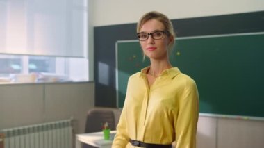 Öğretmen sınıfta tahtaya karşı duruyor. Çekici kadın kameraya bakıyor.