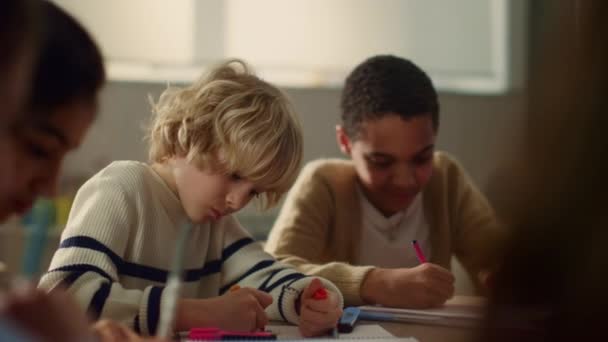 Kinder sitzen am runden Tisch im Klassenzimmer. Schüler zeichnen in Notizbüchern — Stockvideo