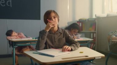 Okulda sıralarda oturan bir çocuk. Elinde kalem tutan düşünceli okul çocuğu.