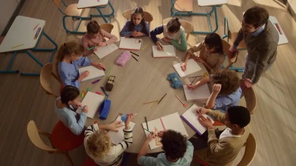 Schulkinder beim Unterricht am runden Tisch. Männlicher Lehrer hilft Kindern beim Unterricht — Stockvideo