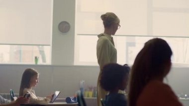 Akıllı öğrenciler dijital tabletlerle çalışıyorlar. Sınıfta yürüyen öğretmen.