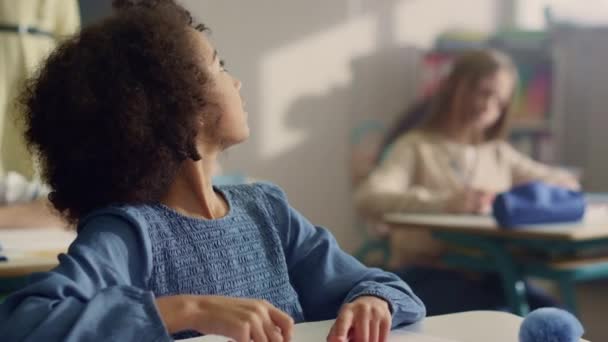 Mädchen hebt die Hand im Unterricht. Lehrerin hilft Schülerin bei Klassenarbeiten — Stockvideo
