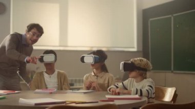 Öğrenciler video gözlük kullanıyor. Öğretmen öğrencilerin aletlerle fen bilgisi öğrenmesine yardım ediyor.