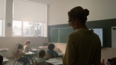 Öğretmen sınıfta öğrencilerle konuşuyor. Okul çocukları birlikte okuyorlar. 