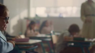 Okul sınıfında sıralarda oturan çocuklar. Öğretmen sınıfta ev ödevlerini kontrol ediyor.