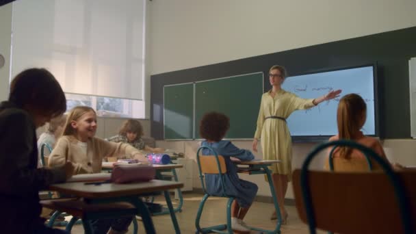 Estudiantes aprendiendo en la escuela primaria. Profesora de pie en pizarra — Vídeos de Stock