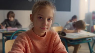 Sınıfta kameraya poz veren ciddi bir öğrenci. Masada oturan neşeli kız. 