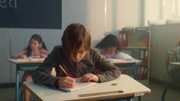 Uczeń piszący w notatniku na lekcji. Przemyślany chłopiec trzymający długopis w ustach — Wideo stockowe