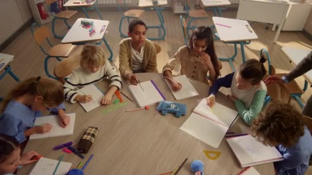 Dzieci uczą się przy okrągłym stole w klasie. Nauczyciel rozmawiający z uczniami — Wideo stockowe
