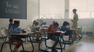 Coronavirüs salgını sırasında tıp maskeli çocuklar sınıfta birlikte ders çalışıyorlar.