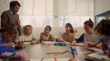 Öğretmen okul çocuklarına ders veriyor. Öğrenciler alıştırma kitaplarına yazıyor. 