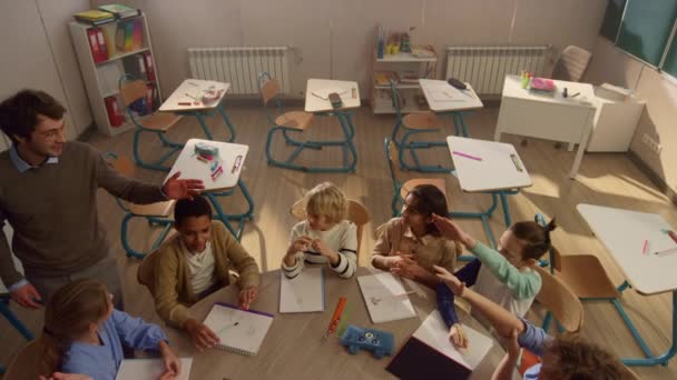 Улыбающийся школьный учитель, объясняющий ученикам урок за круглым столом — стоковое видео