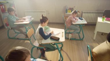 Öğrenciler sınıf çalışması yapıyor. Öğrenciler ve liseli kızlar not defterlerine yazıyorlar.