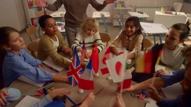Багато етнічних студентів тримають міжнародні прапори в руках за круглим столом — стокове відео