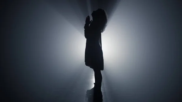 Silhouette imádkozó nő a sötétben. Vallásos lány összehajtogatja kezét az imádságért.. — Stock Fotó