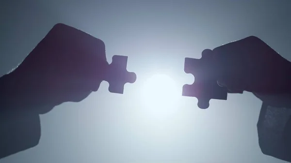 Silhouette hands connecting parts puzzle indoors. Arms matching pieces jigsaw.