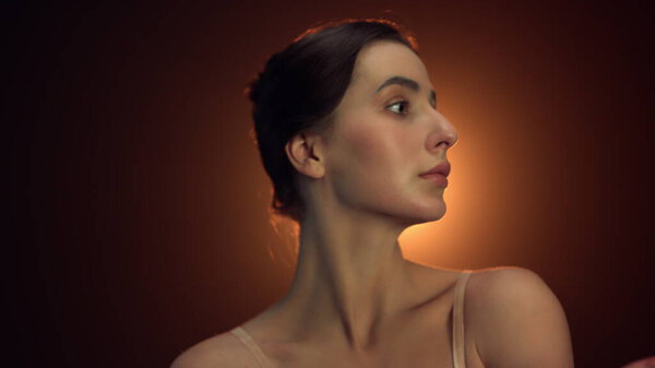 Portrait of tender ballet dancer looking camera in yellow lights background. Closeup beautiful ballerina posing in studio. Natural beauty woman touching neck inside.